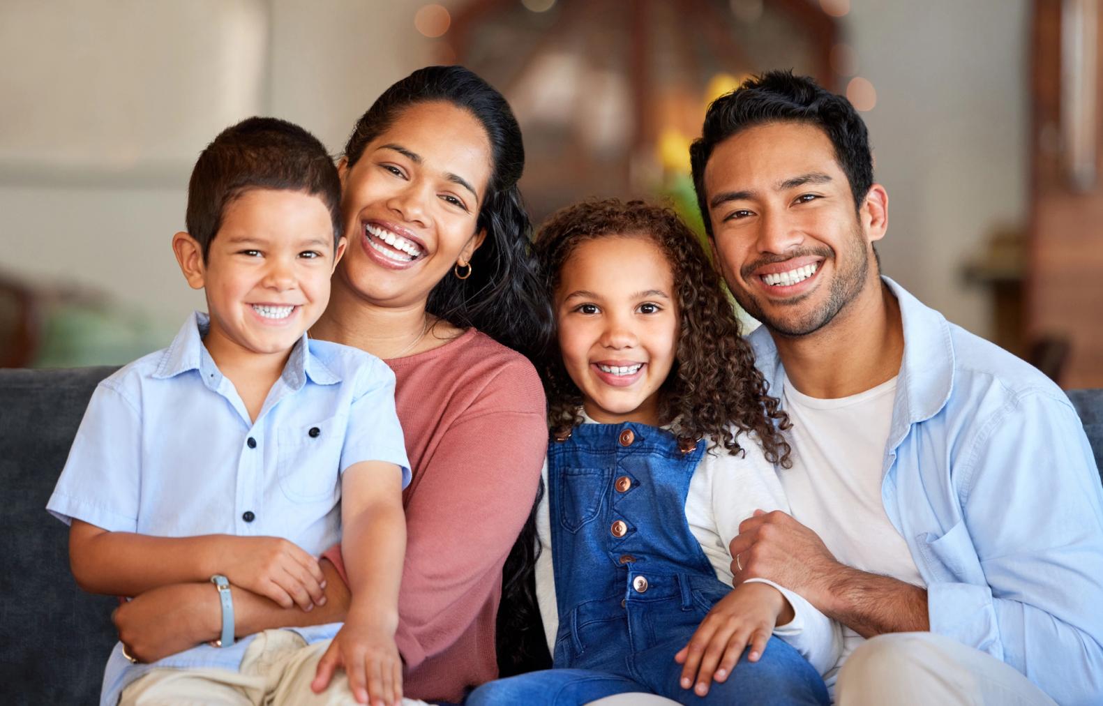 a family is sitting on a couch and smiling for the camera .