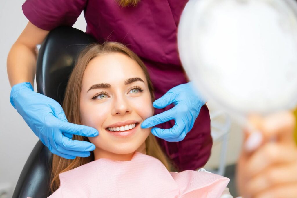 Dentist in blue gloves examining a smiling patient's teeth.