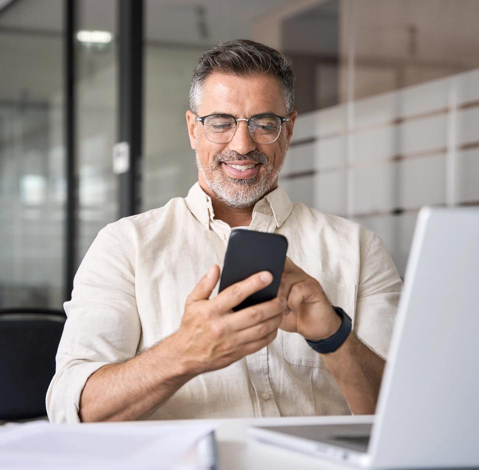 a man is sitting at a desk looking at his cell phone .