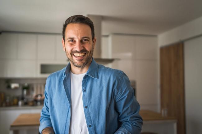 A smiling man in a blue shirt stands in a modern kitchen.