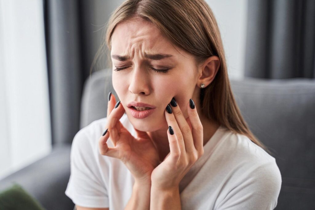 A woman grimacing in pain, holding her jaw/cheek.