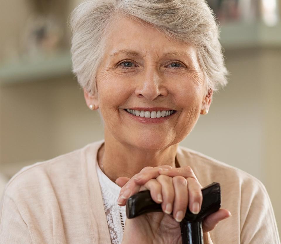 an elderly woman is smiling while holding a cane .